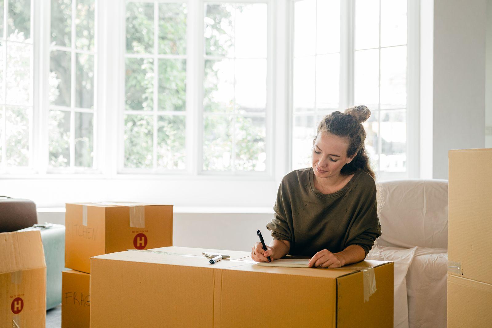 A person labeling a cardboard box in a bright room during a home move.