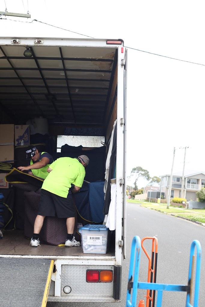 Two movers arranging padded blankets around furniture inside a moving truck.