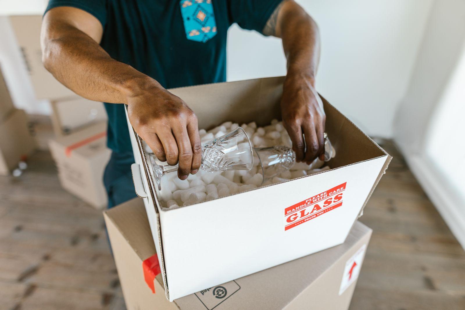 A person packing glassware into a box lined with packing peanuts.